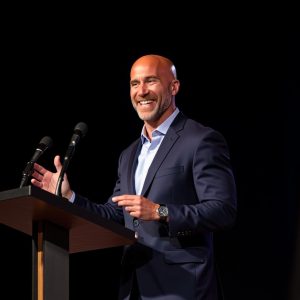 Vince Benevento speaking at a podium about Boys Will Be Men